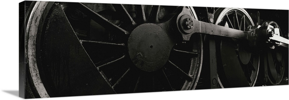 Panoramic photograph displays a monochromatic close-up looking at the components of a train that are attached to the rails.