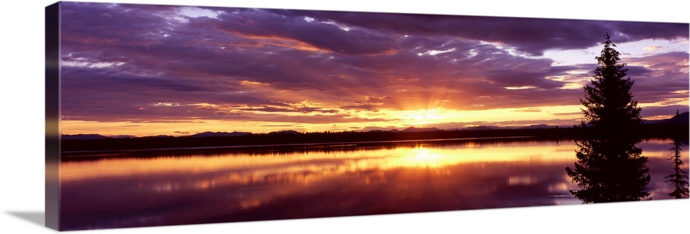 Long horizontal canvas of the sun rising through stormy clouds reflected onto the lake.