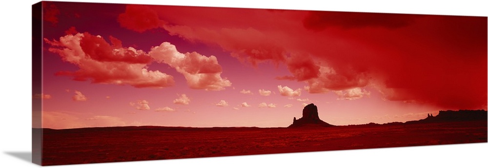 Giant horizontal photograph of a desert landscape beneath a vibrant sky with billowing clouds, a large rock formation on t...