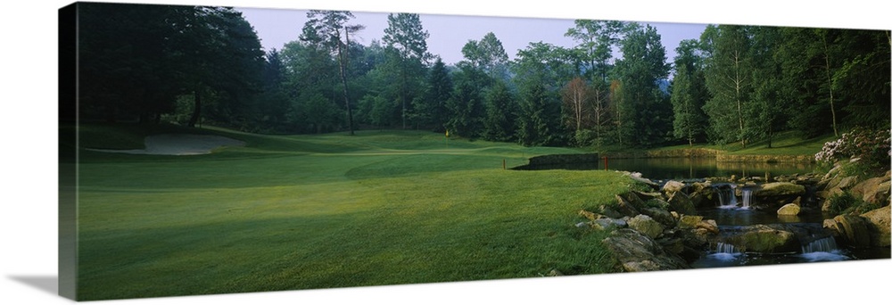 This is a panoramic photograph of a landscaped lawn and trees next to a small cultivated stream.