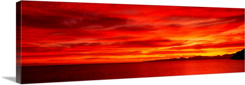 Large wall image of a deep warm sunset over the ocean with a little strip of land on the right side jetting out.