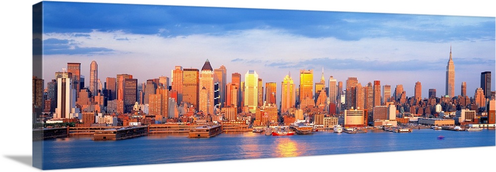 Panoramic photograph taken of the sun as it begins to shine over the New York skyline filled with skyscrapers.  In the for...