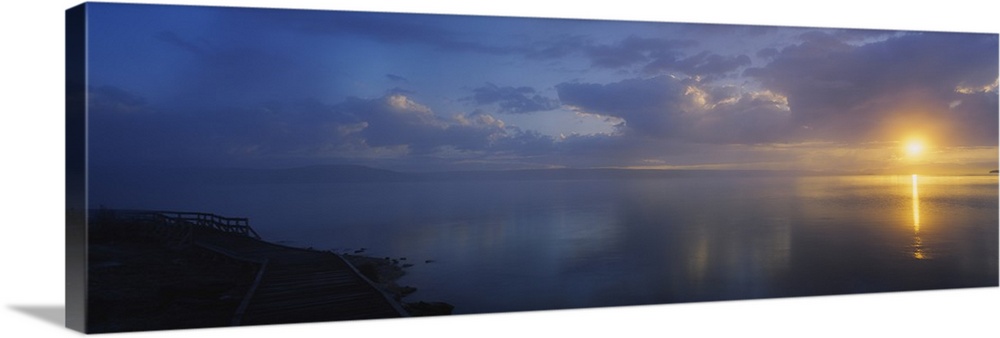 Panoramic photograph of walkway alongside ocean at dawn under a cloudy sky.