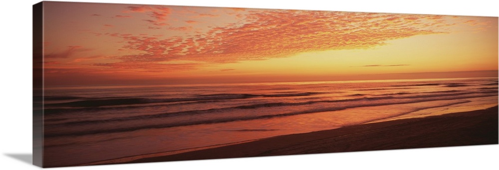 Large, wide angle photograph of a golden sunrise over the Atlantic Ocean, at the shoreline of Daytona Beach, Florida.