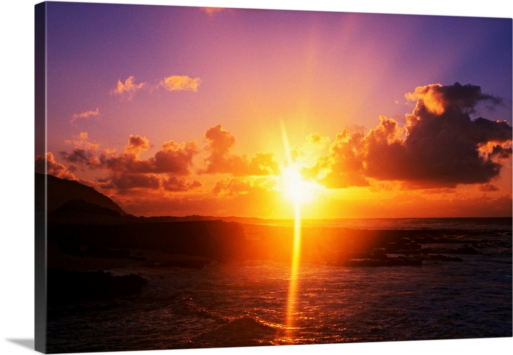 Giant photograph shows a sunrise over Sandy Beach Park in Oahu, Hawaii.  The brightness of the sun can be seen glistening ...