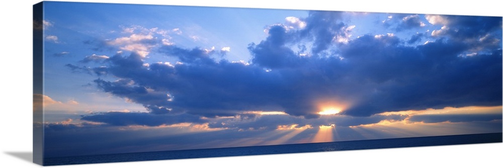 Panoramic photograph of the sun peaking through large, fluffy clouds as it sets over the Gulf of Mexico in Florida.