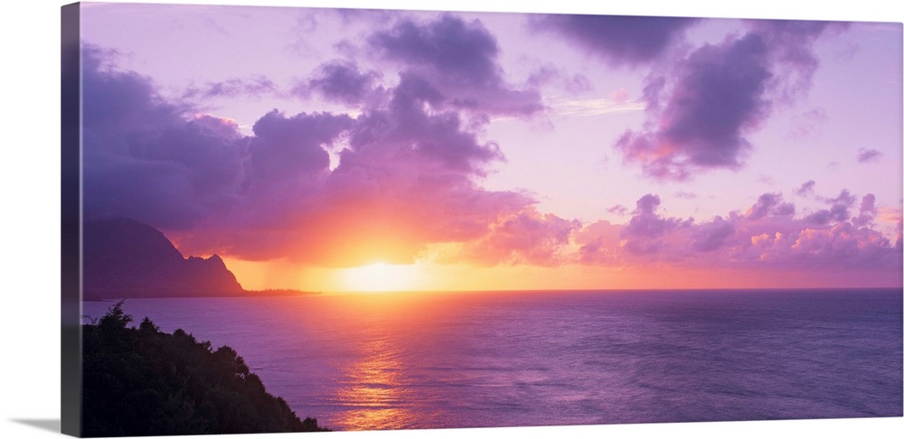 Sun setting on the ocean horizon creating a pastel-colored sky in the evening in Hawaii. Large lavender clouds float above...