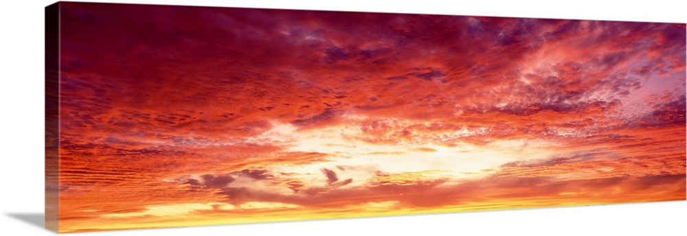 Panoramic photograph of a beautiful sunset sky with warm colored clouds gathered around the sun.