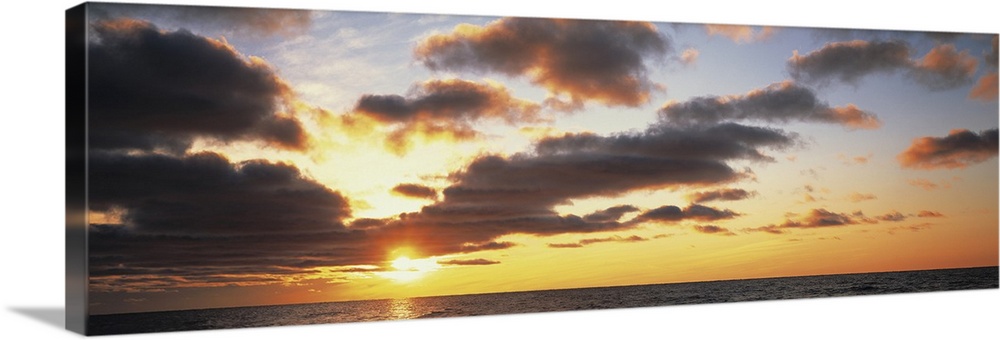 Wide angle photograph of the sun setting slightly behind clouds, over the vast waters of Lake Michigan.