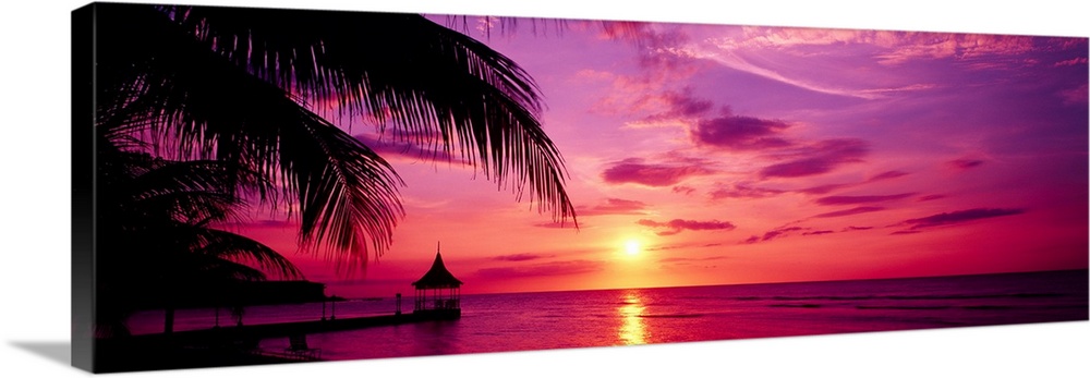 Panoramic photograph of a colorful sunset on the beach in Montego Bay, Jamaica.  The palm trees and dock in the foreground...