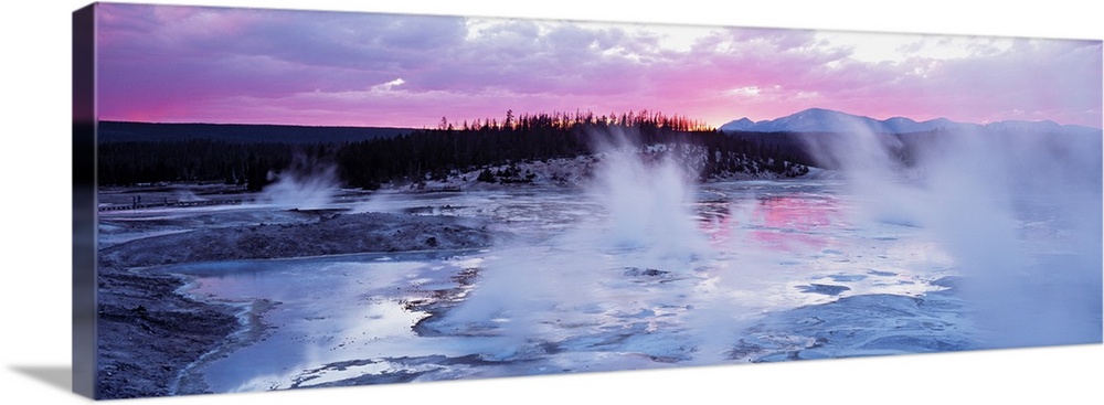 Large panoramic piece of geysers in Wyoming as the sun sets in the distance and gives the sky pink and purple hues.