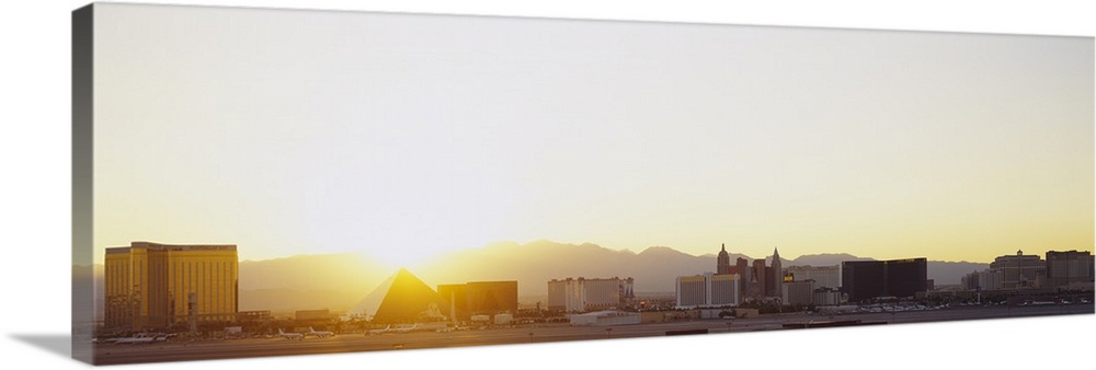 Panoramic picture taken of the strip in Las Vegas with a bright sun setting behind the mountains in the distance.