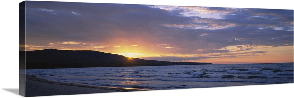 Panoramic canvas photo of waves crashing in the ocean and a setting sun peeking through a rolling mountain.