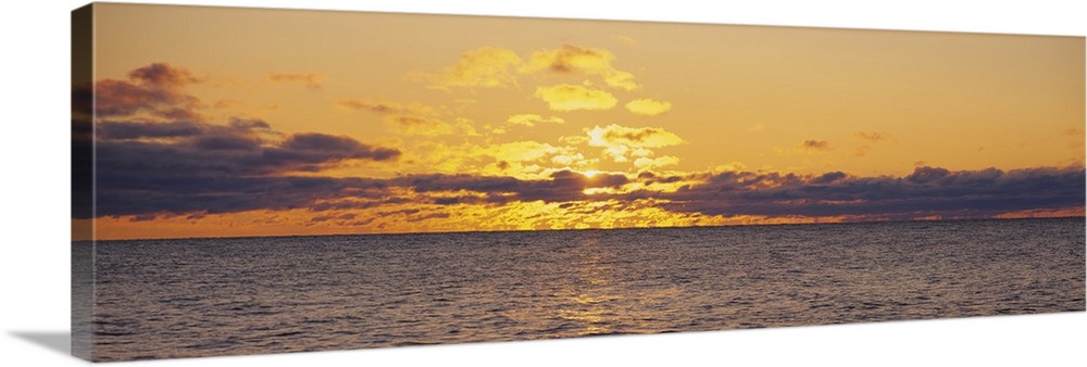 Panoramic photo on canvas of a sunset shining through clouds above a lake.