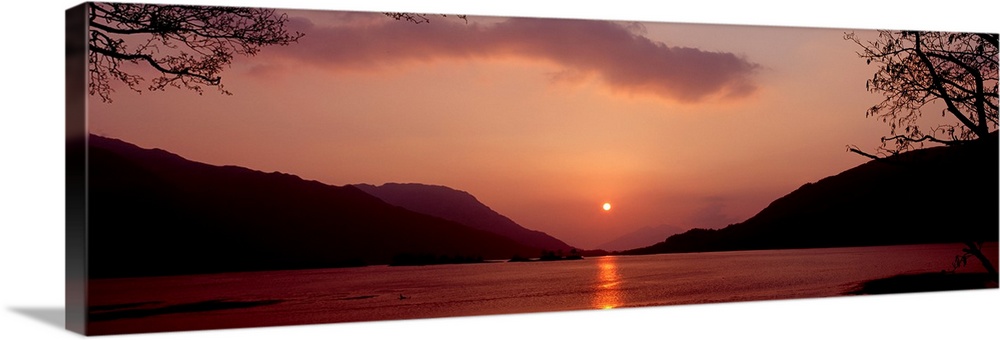 Panoramic photo on canvas of a sunset over the water with rolling hills in the background.