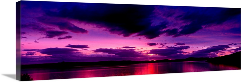 A panoramic photograph of clouds in the sky and light reflecting off water in the twilight colors.