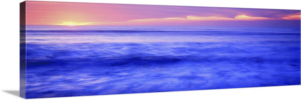 Panoramic photograph shows the sun setting over the horizon and sparkling over a coast of the Western United States.