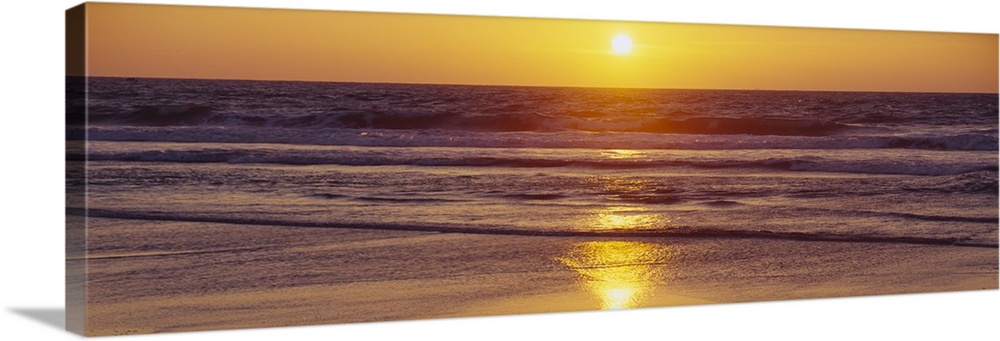 Panoramic photograph of ocean at dusk with sun reflected in water.