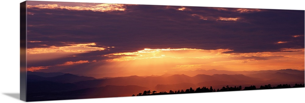 Wide angle photograph of the sun setting behind a cloudy sky, over the distant Rocky Mountains.  Taken from Daniels Park i...