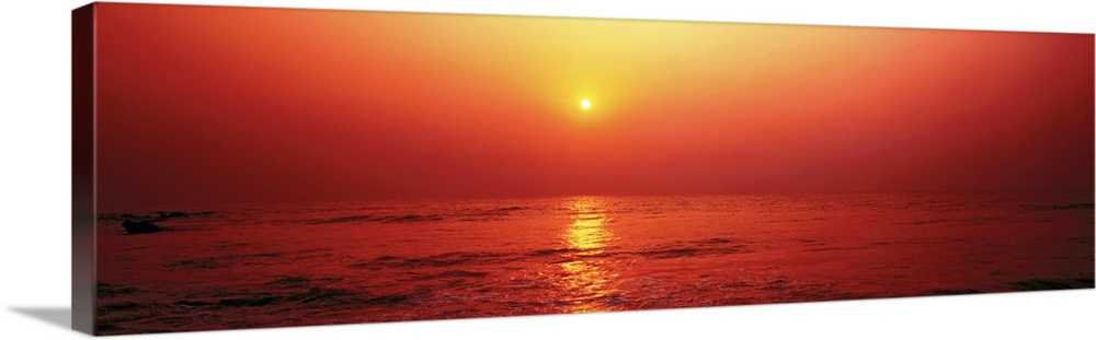 Panoramic photograph taken of the sun as it begins to set in the sky. The entire picture has a warm tone to it.