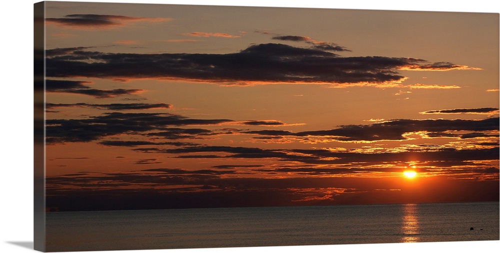 A seascape panoramic photograph of sunlight reflecting on water and clouds on the New England coast.