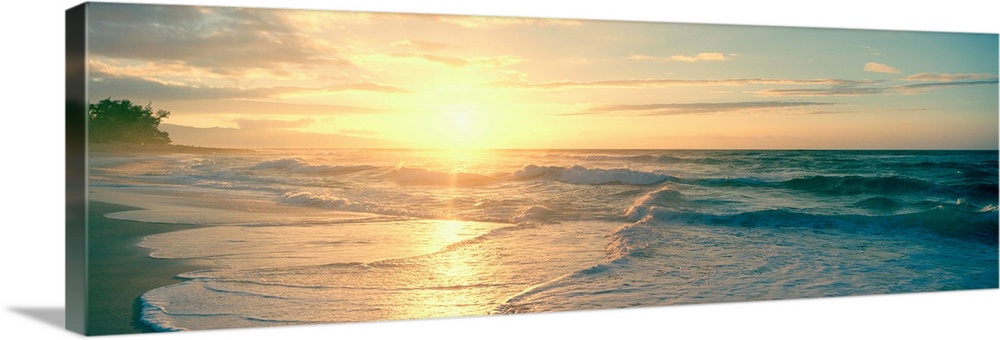 Long panoramic print of an intense setting sun going down over the ocean with waves washing ashore on the left.