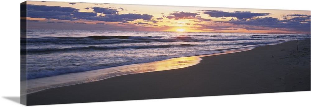 The sand and ocean are pictured in wide angle view with the sunset off in the distance.