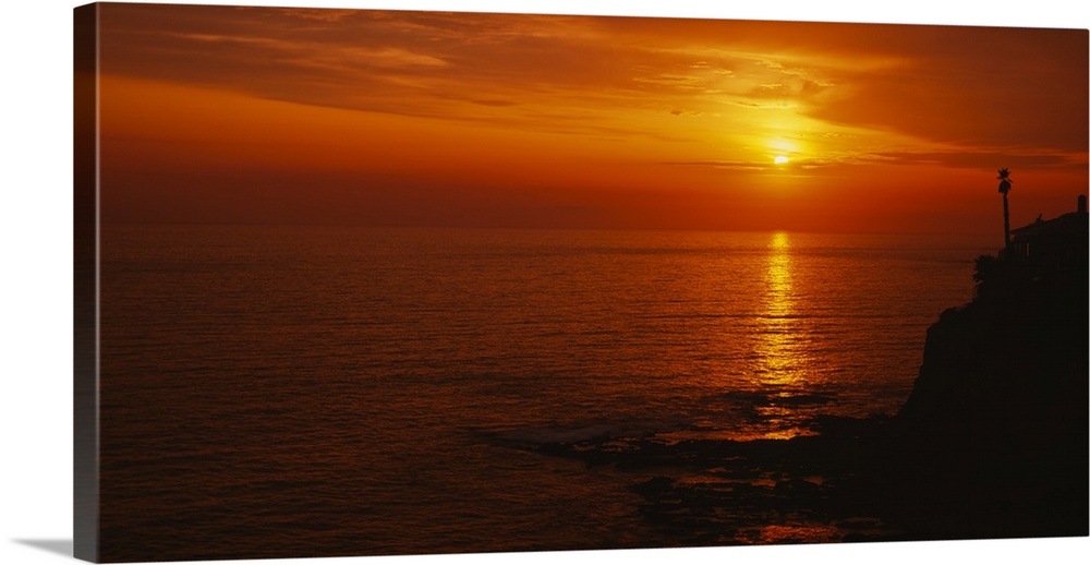 Landscape, large wide angle photograph of a fiery sunset over calm waters at Laguna Beach in California.