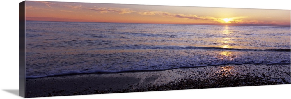 This is a panoramic landscape photograph of waves softly washing up on the shore of a sandy beach.