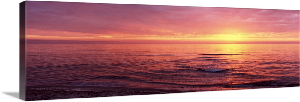 Panoramic photograph of sun setting over ocean at dusk.