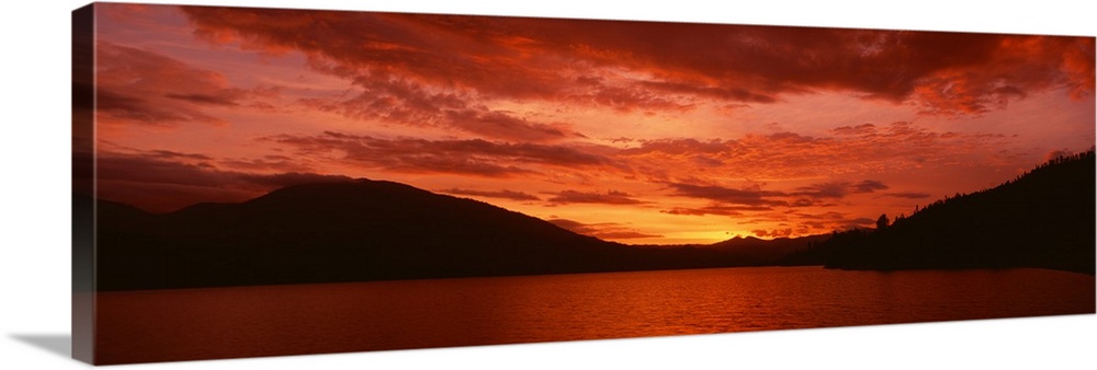 Panoramic photograph of a vibrant fiery sunset over a silhouetted mountain landscape and Whiskeytown Lake in California.