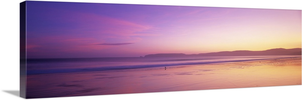 This large panoramic piece shows a sun setting behind vast hills over the Pacific ocean.