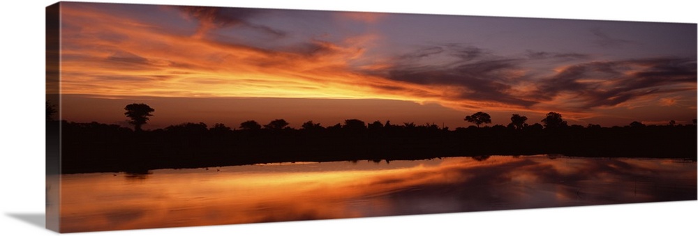 Panoramic photo on canvas of a bright sunset along a river in Africa with a tree line silhouetted against the sky.