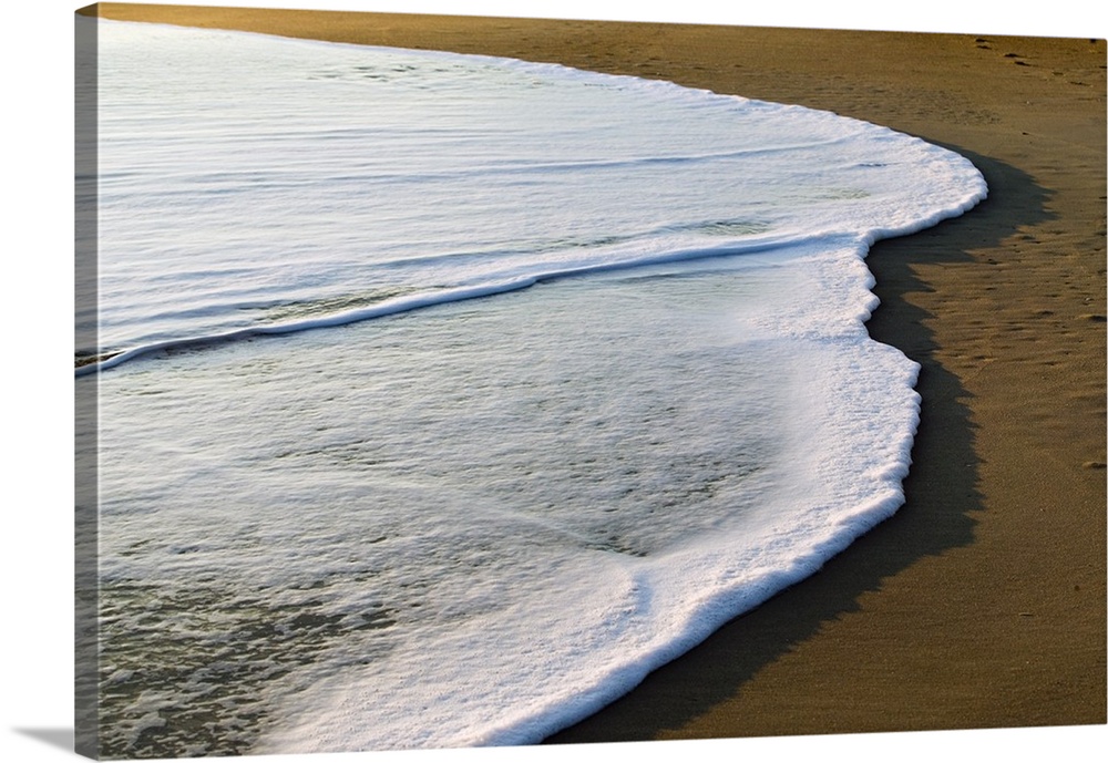 Horizontal, large photograph of the white surf covering part of the sand on a beach of the Outer Banks in North Carolina.