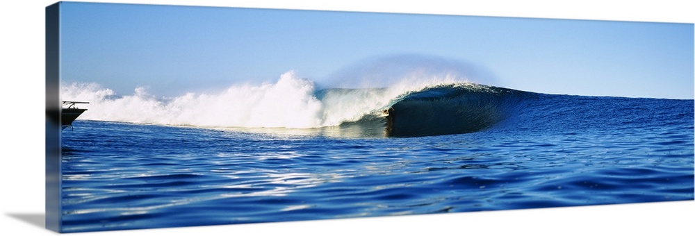 Large, horizontal photograph of a distant surfer riding a large wave, in the blue waters of Tahiti, French Polynesia.