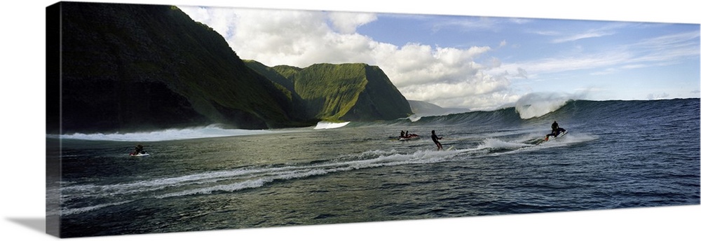 This is a panoramic photograph of ocean swells and volcanic cliffs and surfers waiting to catch the next wave.