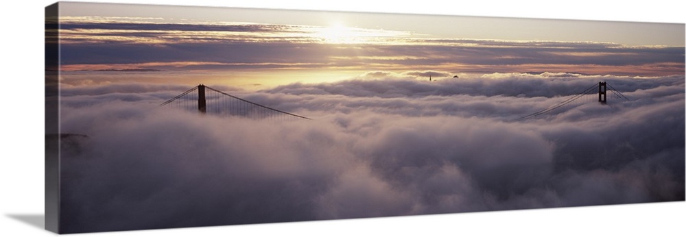Panoramic photo of the tops of the Golden Gate Bridge peeking through the dense fog.