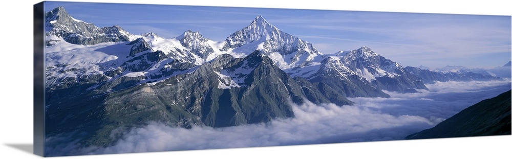 Panoramic, aerial photograph of thick clouds surrounding the snow capped Swiss Alps, against a blue sky, in Switzerland.