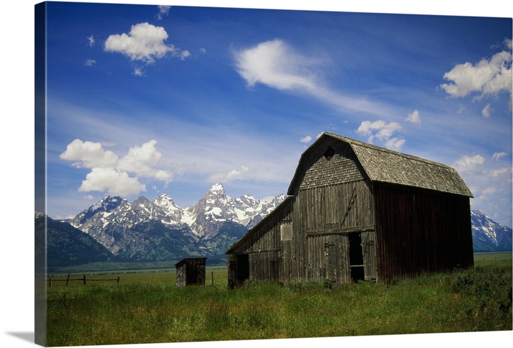 Large photograph of a rustic barn in a grassy field with a mountain range behind it in Grand Teton National Park, Wyoming.