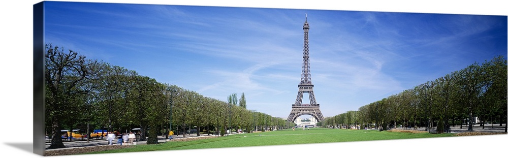 Tree lined grassy field in Paris with the Eiffel Tower protruding in to the clear blue sky.
