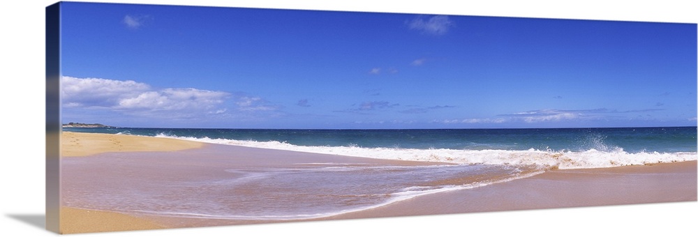 This is a landscape panoramic photograph of a flat sandy shoreline and a calm sea with few clouds in the sky.