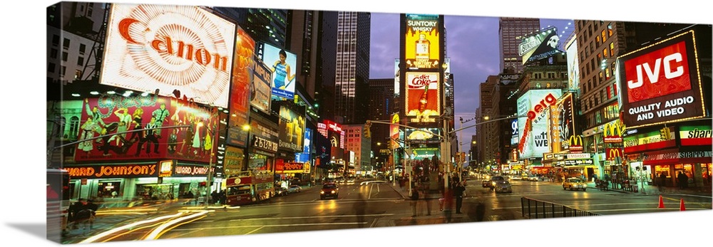 Wide angle photograph of Times Square in New York City, lit at night, with billboards including Canon, JVC, and Diet Coke.