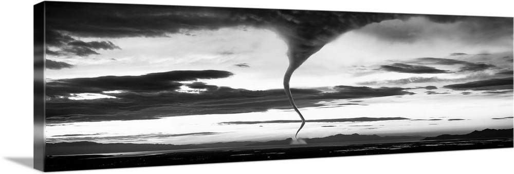 Panoramic photograph of funnel cloud reaching down to earth surrounded by a dark, cloudy, stormy sky.