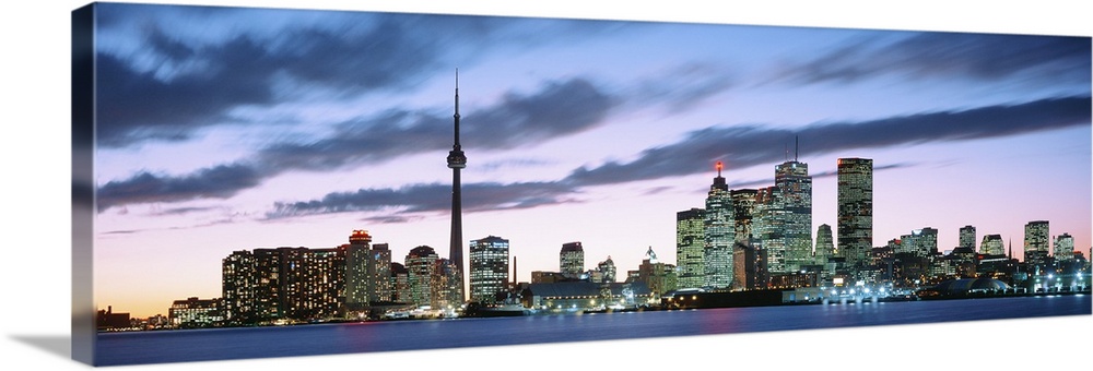 Panoramic photograph of the modern city of Toronto at twilight, under dark clouds in a pastel sky lit up by the sunset.