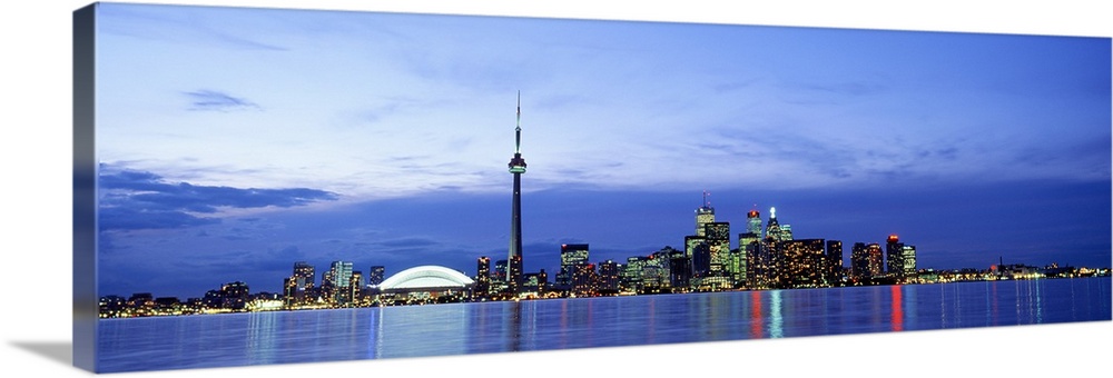 A wide angle photograph taken of an illuminated skyline in Canada at dusk. The lights reflect in the water shown in front ...