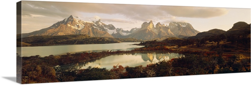 Big, landscape, wide angle photograph of snow covered mountains behind waters surrounded by forest, in Torres del Paine Na...