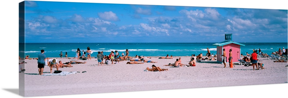 Long horizontal print of people out and about on the beach with crashing waves behind them.