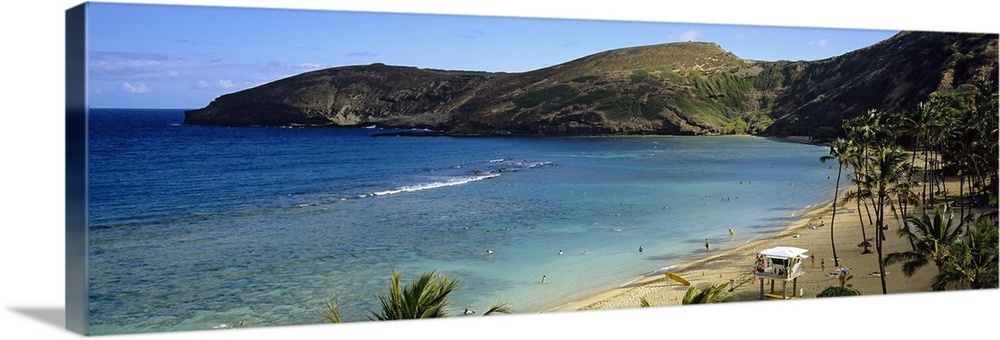 Wide angle photograph taken on a beach in Hawaii that is surrounded by mountainous terrain and shows people in the ocean.