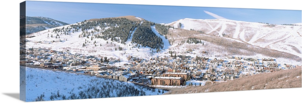 Wide angle photograph on a large canvas of a distant town in a valley, surrounded by a snow covered mountain landscape in ...