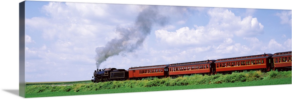 Panoramic photograph on a large canvas of a steam train with red cars moving down a track surrounded by a green field, ben...